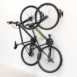 Two bicycles are hung vertically on a clean white wall using a black wall-mounted bike rack that swivels, allowing the bikes to lay flat against the wall to save space.
